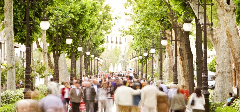 Crowd walking down a city street lined with trees