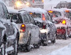 Cars are stuck in traffic on a snow-covered road during heavy snowfall, with snow piling up on vehicles