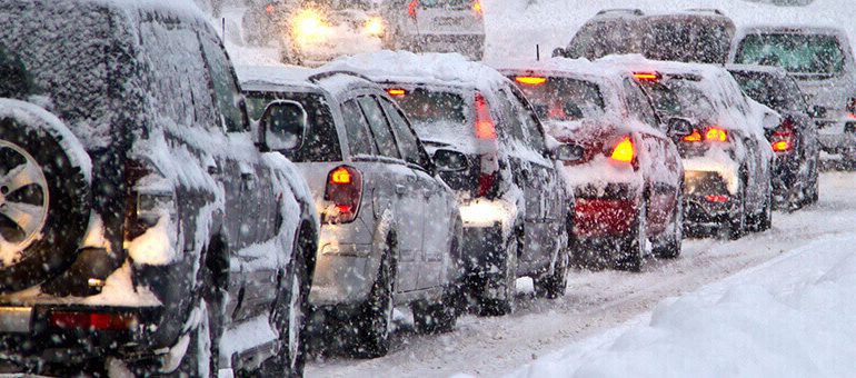 Cars are stuck in traffic on a snow-covered road during heavy snowfall, with snow piling up on vehicles