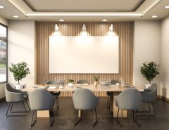 A conference room with a large empty rectangular frame mounted on a wood-paneled wall above a long table surrounded by six grey chairs.