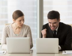 A woman looking surprised at her laptop while a man in a suit clenches his fist in celebration at his own laptop.